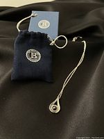 Full view of necklace with pendant and branded pouch, displayed on black fabric background