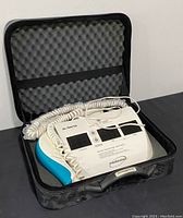 Solaris Medicolux compact light therapy device with dual screens and coiled wires placed in open hard protective zippered case with foam padding.