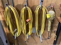 Three yellow extension cords hanging coiled on hooks on a wooden wall.
