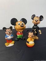 Four vintage Mickey Mouse collectibles arranged on black surface, showing various sizes and styles.