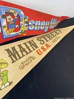 Red Walt Disney World pennant with Mickey Mouse, Minnie Mouse, Donald Duck, and Pluto characters visible along with beige Main Street USA pennant with classic Disney characters.