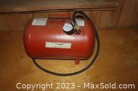 Side view showing red metal portable air tank with attached hose and pressure gauge on top