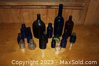 View of multiple antique bottles on wooden surface, mostly cobalt blue bottles with some brown and clear bottles mixed in.