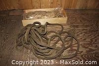 Large coil of thick antique hemp rope laid on a wooden floor with a cardboard box behind it containing smaller twine coils.
