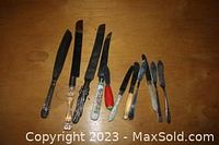 Eight assorted butter and cake knives laid out on a wooden surface, showing different handle designs and blade shapes.