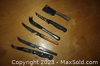 Top-down view of six cheese cutting tools showing various blade types and handles on wooden surface.