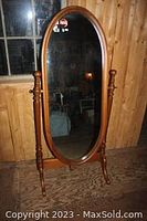 Full view of the oval cheval mirror in pine frame against wood panel wall, showing height and structure