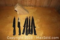Set of six black handle knives displayed with wooden knife block on a wooden surface.