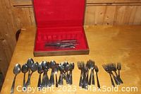 Full set of spoons, forks, knives arranged in front of an open red flatware storage case with slots for knives.