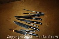 Photo showing nine silver-handled kitchen tools including various knives and a carving fork laid flat on a brown surface.