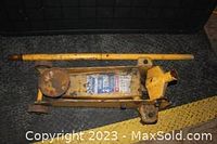 Photo of the entire yellow 2 ton floor jack with long handle laid alongside it, showing rust and worn paint.