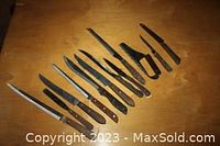 Top view of 12 large kitchen knives arranged on a wooden surface, showing different blade types and wooden handles.
