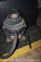 Full view of black Shop-Vac wet/dry vacuum with hose and attached nozzle, showing overall condition and branding.