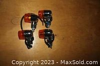 Four small orange-lensed lights mounted on chrome-metal brackets designed for small boat or trailer use on a wooden surface.