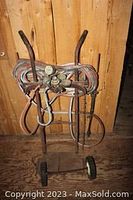 Full view of the metal cart holding coiled welding hoses and torches with two handles and missing wheels