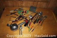 Wide shot displaying all kitchen utensils spread on wooden surface, illustrating variety and quantity of vintage utensils including ladles, manual hand tools, and a meat tenderizer hammer.