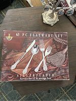 Box cover showing the food service utensils laid out on the front with the text '63 PC Flatware Set, Silverplated, Service for 12 & storage box'.