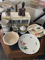 Photo shows various ceramic kitchenware including tea cups, sugar bowl, creamer, salt and pepper shakers, and serving plates arranged for display.