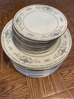 Stacked set of 12 dinner plates and 12 butter plates showing floral and scroll decorative pattern on white china.