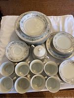 Photo showing entire china set including dinner plates, lunch plates, butter plates, cups, saucers, bowl, and sugar bowl arranged on a tablecloth.