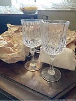Pair of clear crystal red wine goblets with detailed cut patterns on the bowl and faceted stems, placed on a wooden table with crumpled paper around.