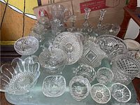 Full lot of 36 clear crystal pieces including bowls, pitcher, candle holders, and serving utensils arranged on a glass table.