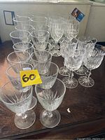 Photo showing the full set of 26 crystal wine goblets arranged on a wooden surface with a yellow bidding tag.