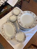 Photo showing stacked dinner plates, saucers, oval platters, and butter plates with a floral border pattern on white porcelain.