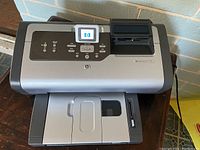 Front view of HP PhotoSmart 7760 printer showing control panel with LCD screen and paper trays.