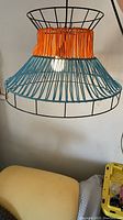 Close-up of one IKEA Modern Idea hanging lamp showing colorful wireframe metal shade in orange, blue, and black colors.