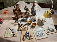 Photo showing the complete collection of vintage figurines including Native American figures, cowboy, cows, pig scent diffuser, orange leaf bowls and four decorative ceramic tiles on a white cloth background.