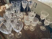 Photo showing 22 assorted crystal glasses placed on a wooden table with various shapes and styles including champagne flutes, wine glasses, and other stemware.