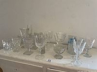Photo showing multiple pieces of glassware in different shapes and sizes on a white surface against a plain wall.