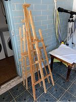 Four wooden painting easels standing upright showing adjustable support and natural wood finish.