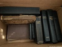 Photo showing seven vintage religious books in a cardboard box, varying in size and condition, primarily black and brown leather covers.