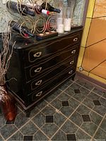 Photo of black wooden dresser with curved four drawers and ornate gold handles, holding wine bottles and candles
