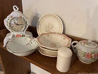 Group photo of vintage porcelain clock, three decorative bowls, sugar bowl, and salt shaker on wooden shelf.