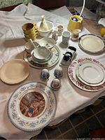 Photo showing assortment of vintage plates, cups, bowls, decorative vases, butter dish, salt and pepper shakers, and citrus juicer