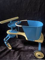 Side view of the 1950s blue metal stroller/walker showing the bucket seat, handle and front wheel.
