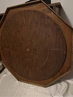 Photo showing octagonal wooden crokinole board flat with visible concentric scoring rings, small pegs, and worn edges
