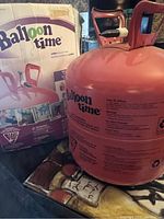 Photo of the pink Balloon Time helium tank next to the original box showing tank shape and handles.