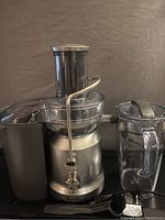 Front view of the Breville juicer showing the main base, feed chute with metal lid, pulp container, and included brush accessory.