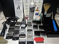 Photo showing Andis clipper, various blades, blades holders, oils, brushes, combs, and black plastic organizer compartment.