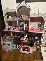 Full view of large multi-story dollhouse with dolls, furniture, and a small white and pink car visible at the base.