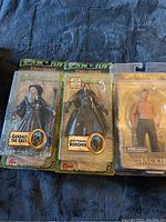 Three figurines in original manufacturer packaging on a blue fabric background. From left to right: Gandalf the Grey with grey robes and staff, Super Poseable Boromir with armor and weapons labeled with '30 points of articulation', and Jacob Black shirtless from Twilight New Moon in clear plastic blister packs.