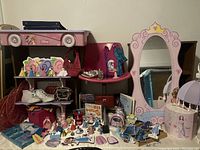 Photo showing two-tier white shelf with Disney cartoon decorations, pink swivel chair, pink princess mirror, jewelry box, and numerous Disney princess and character figurines along with small purses and other children's items on surface below