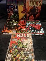 Seven Hulk comic books arranged together on a dark surface showing various titles and colorful cover art depicting Hulk in different forms