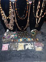 Full lot view including beaded necklaces on bust displays, assorted loose beads in bags, carved wood jewelry and peacock feather design pendant.