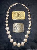 Full view of the heavy metal bead necklace and two metal belt buckles on black background