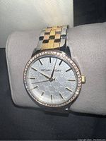 Front view on cushion showing silver monogram dial, crystal bezel, multicolor bracelet